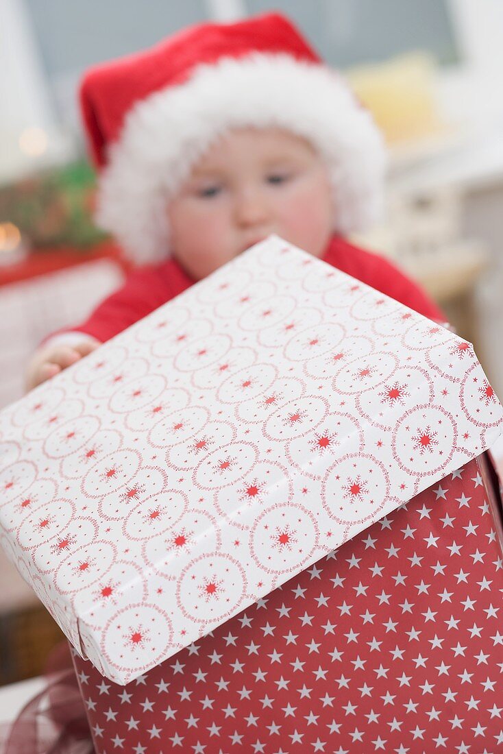 Baby in Father Christmas hat opening Christmas parcel