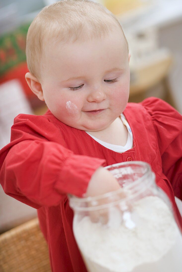 Toddler reaching into jar of flour