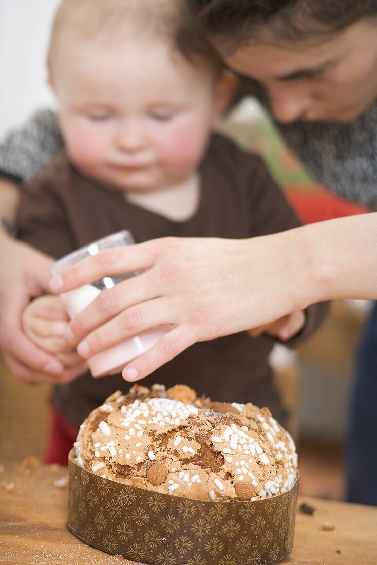 Mutter und Kleinkind streuen Zucker auf Mandelkuchen