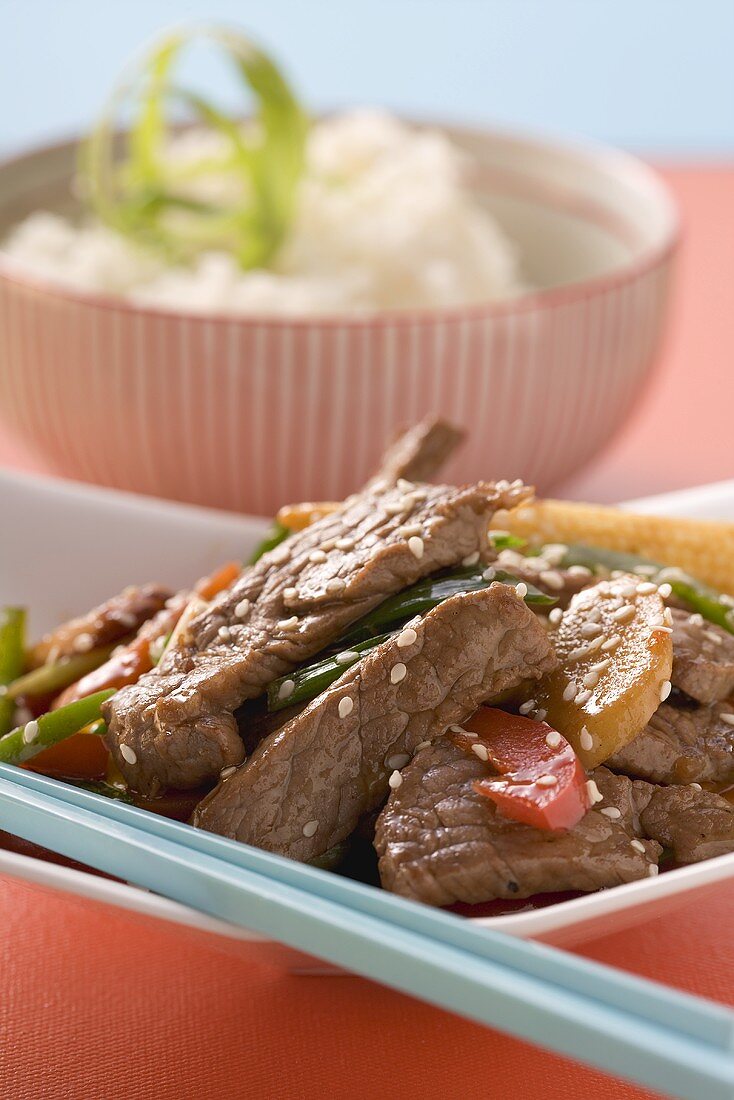 Beef with vegetables & sesame seeds, rice in background (Asia)