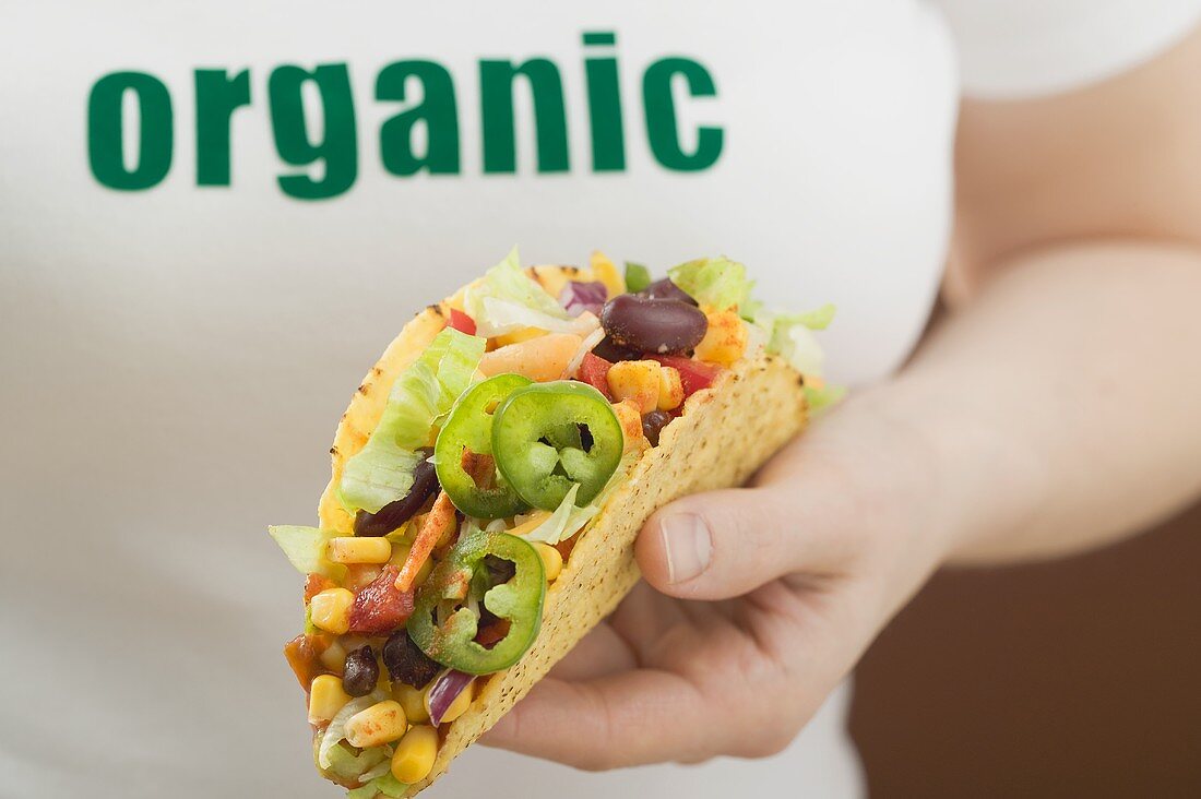 Hand hält Taco mit Gemüsefüllung