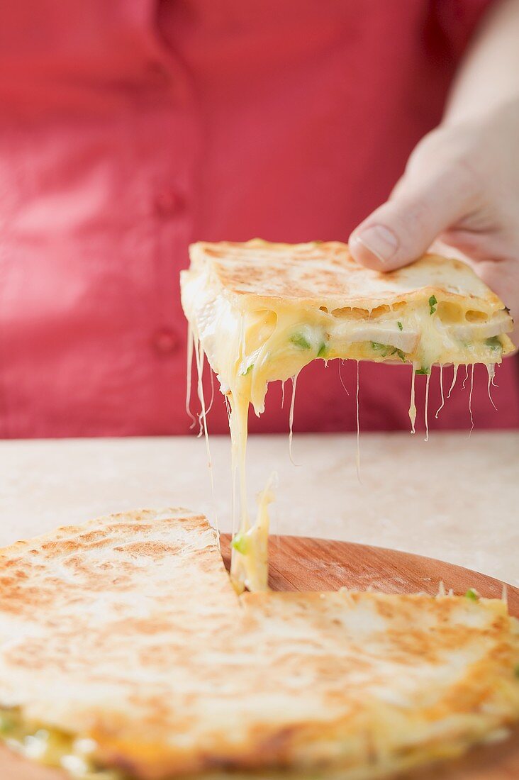 Hand taking piece of quesadilla from wooden board