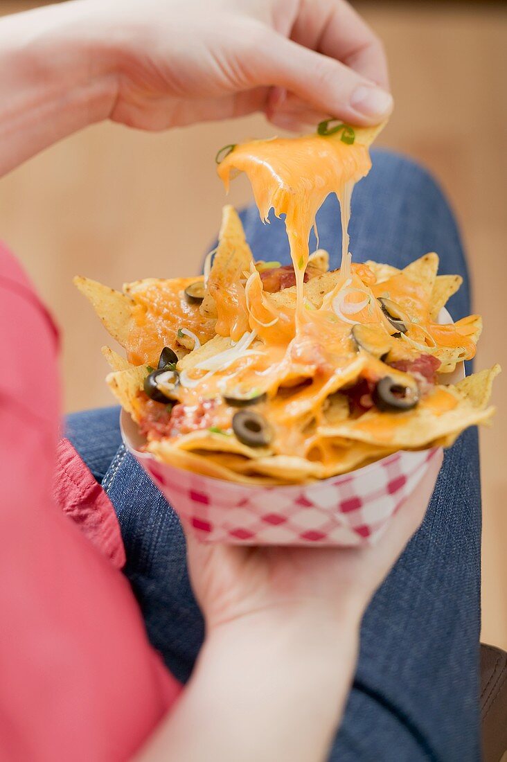 Hand taking nachos with melted cheese from cardboard container
