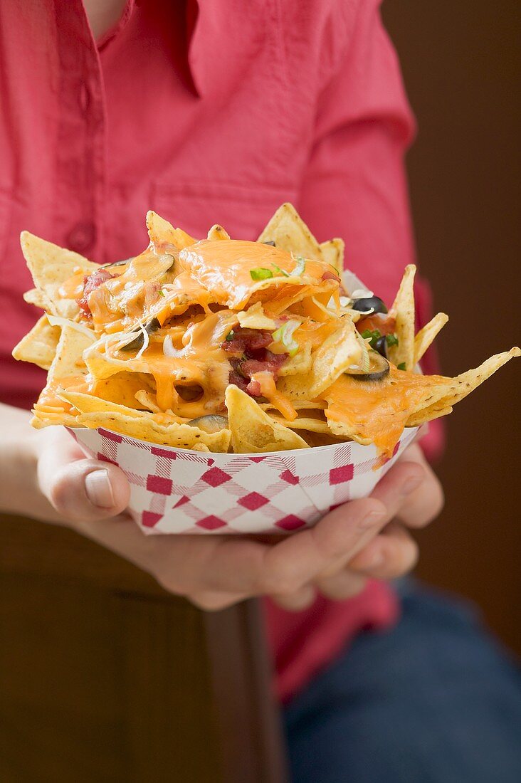 Woman holding nachos with melted cheese in cardboard container