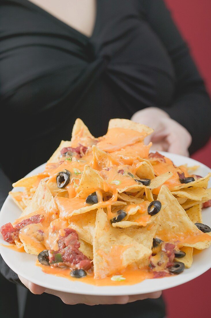 Woman holding plate of nachos with melted cheese