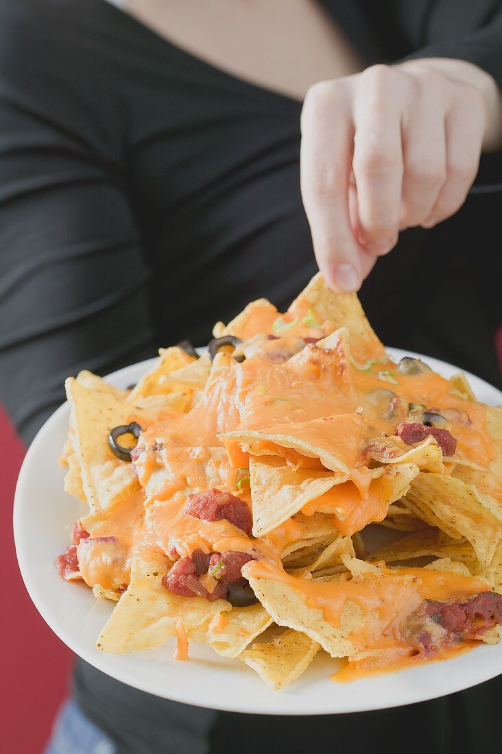 Frau greift nach überbackenen Nachos auf Teller