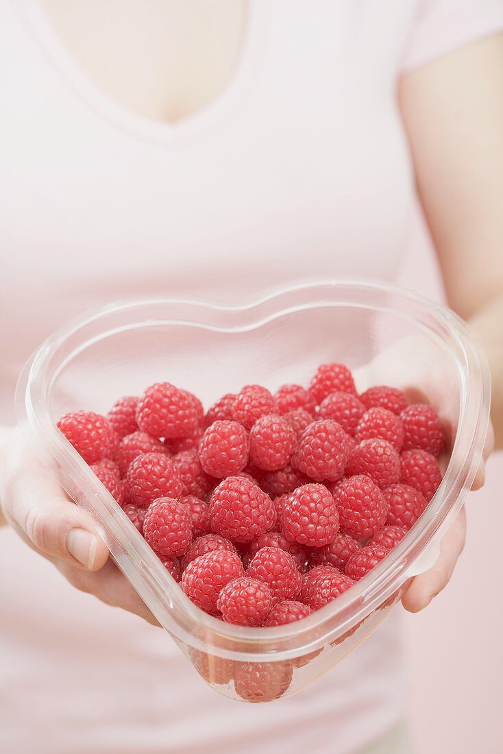 Woman holding heart-shaped container of raspberries