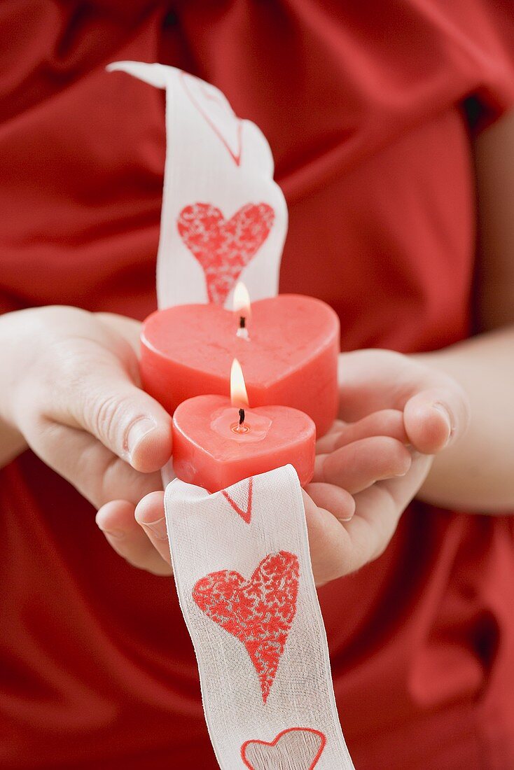 Hands holding two heart-shaped candles on ribbon