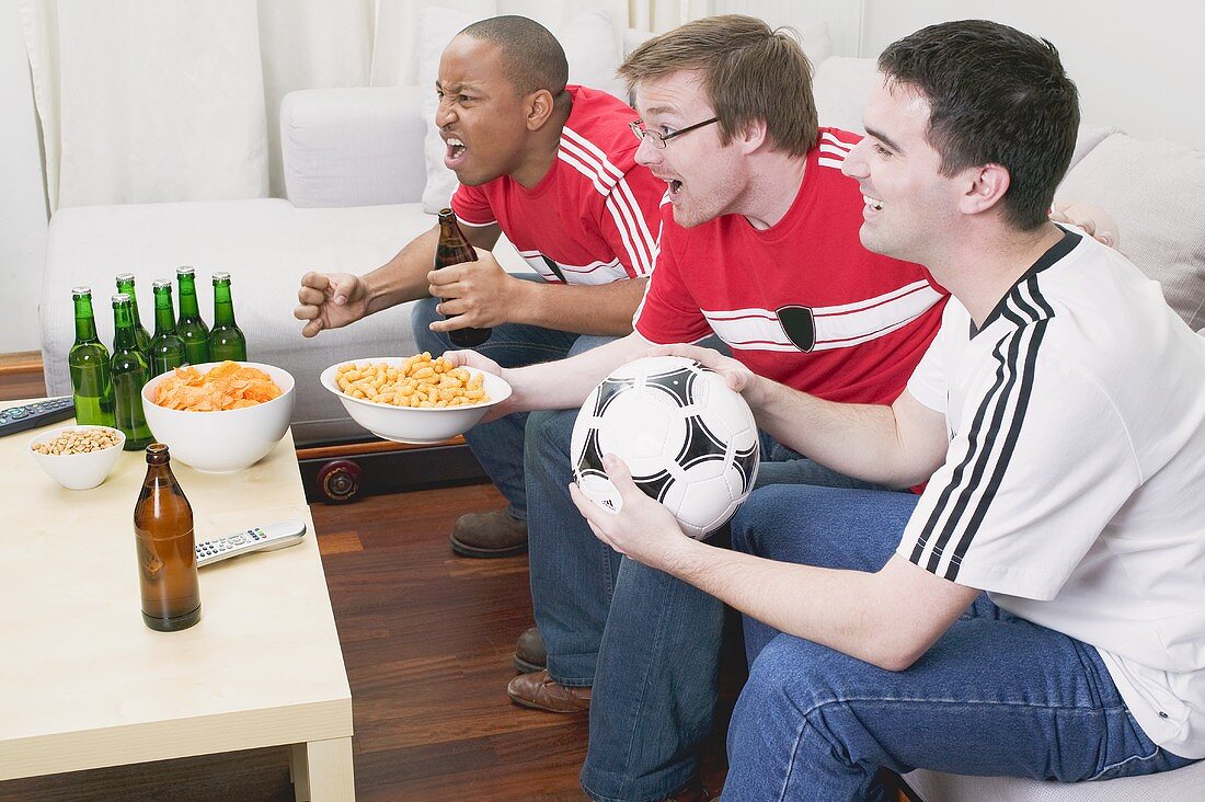 Three football fans with nibbles and beer watching TV