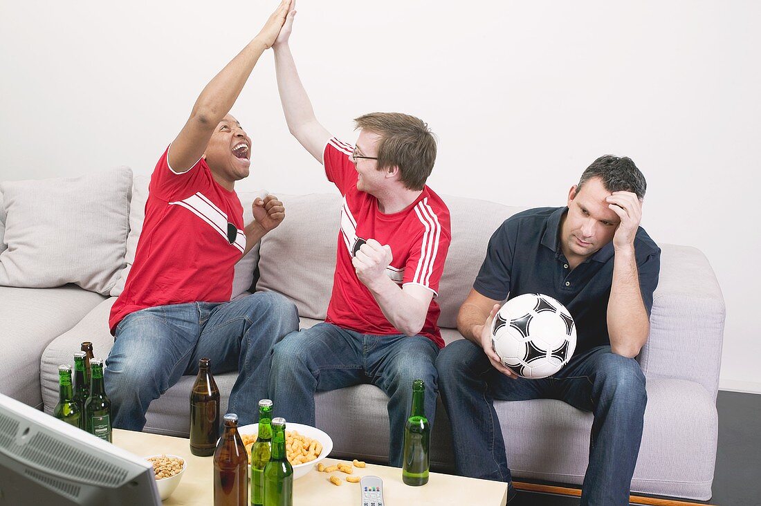 Three football fans, disappointed and excited, watching TV