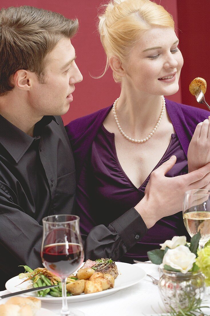 Woman tasting roast potato from her partner's plate