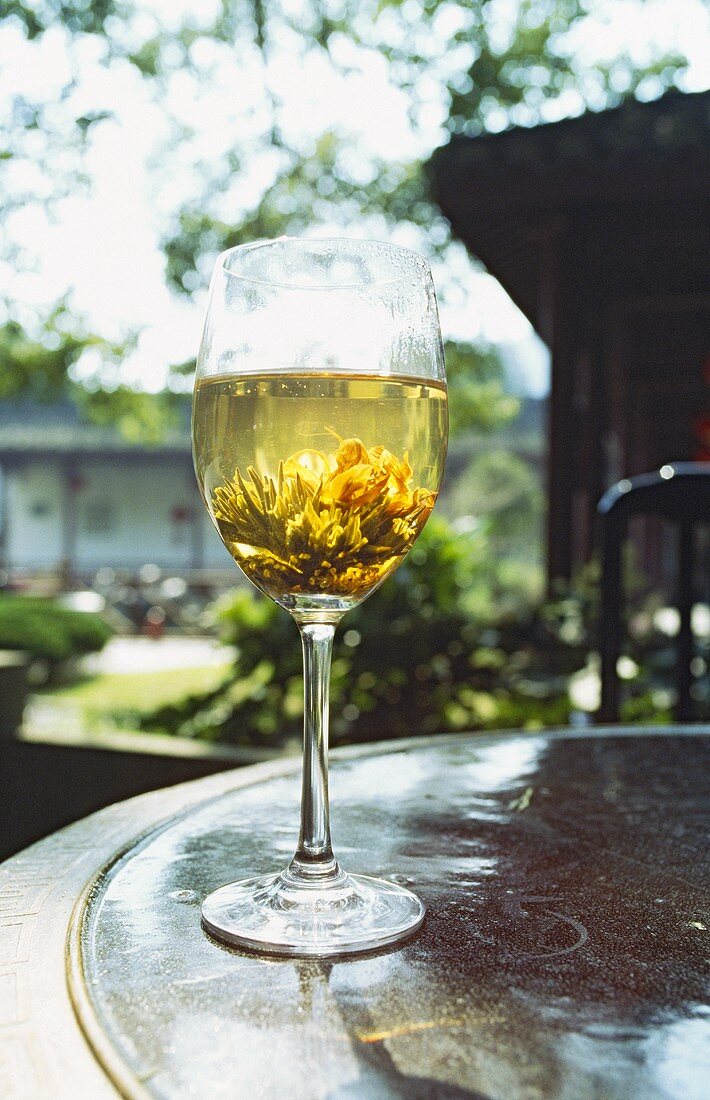 Tee mit Teerose im Glas auf Tisch im Freien