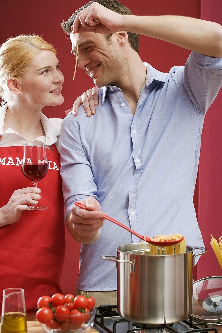 Paar kocht Spaghetti mit Tomaten, Frau hält Glas Rotwein