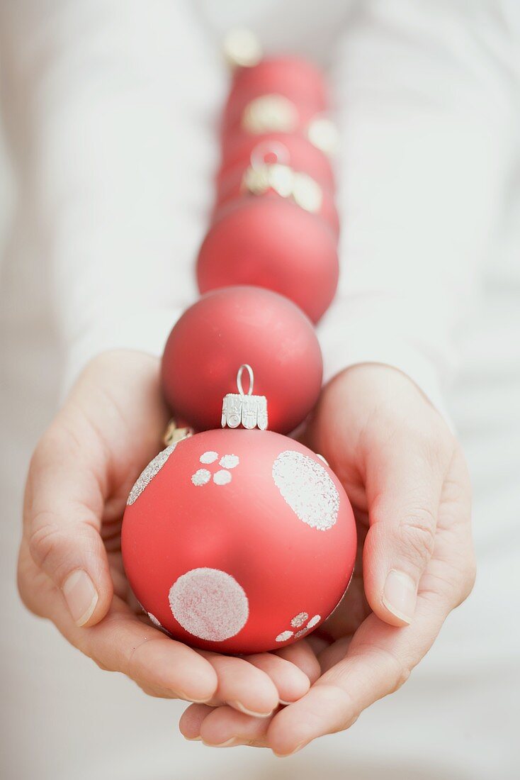 Hände halten rote Christbaumkugeln