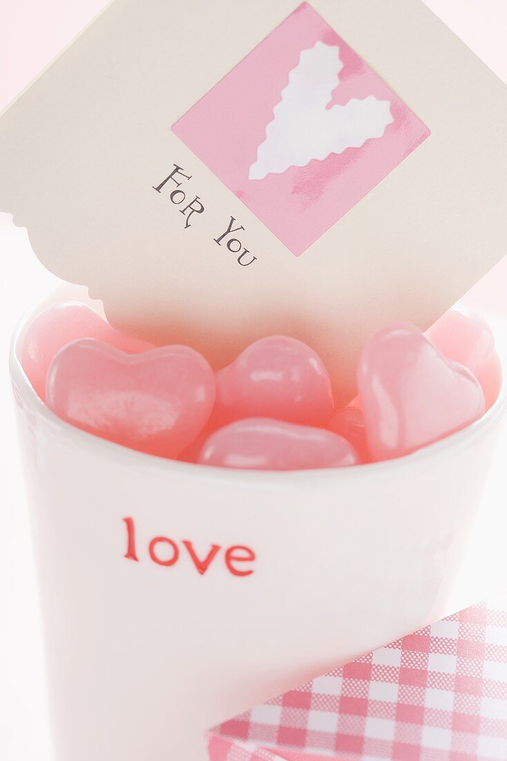 Pink heart-shaped sweets & card in beaker for Valentine's Day