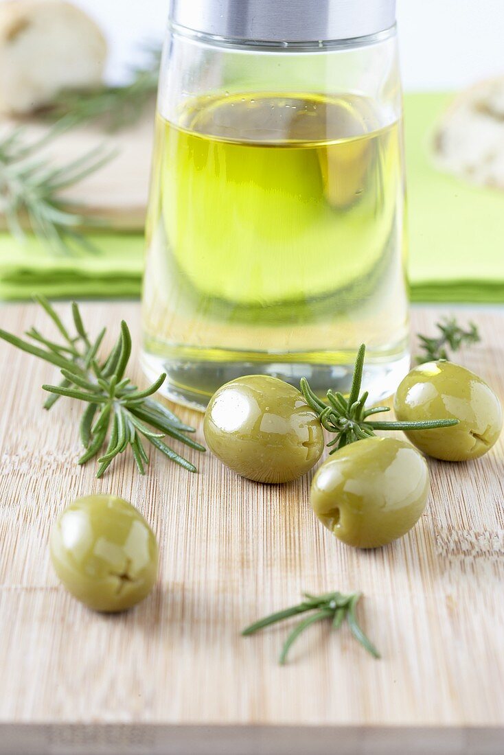 Olivenöl, grüne Oliven und Rosmarin auf Schneidebrett