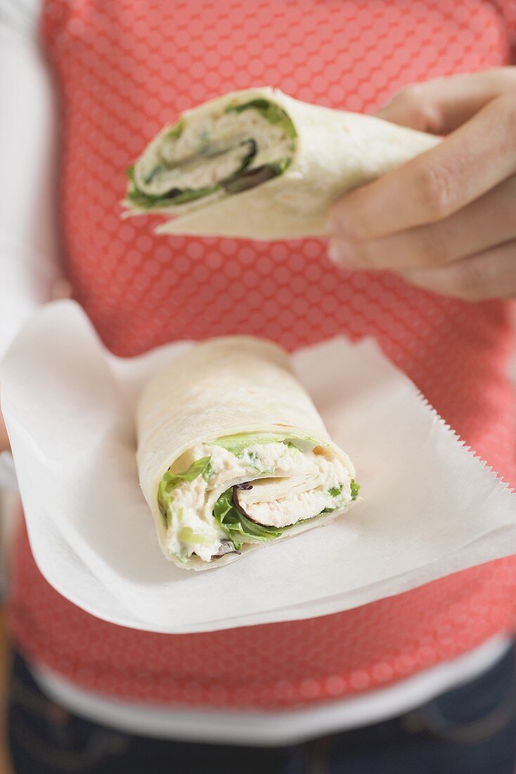 Woman holding two tuna wraps on paper