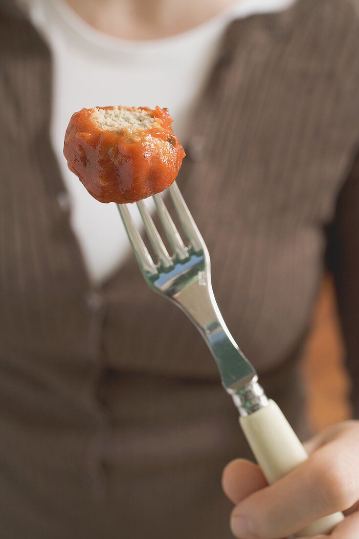 Woman holding partly-eaten meatball on fork