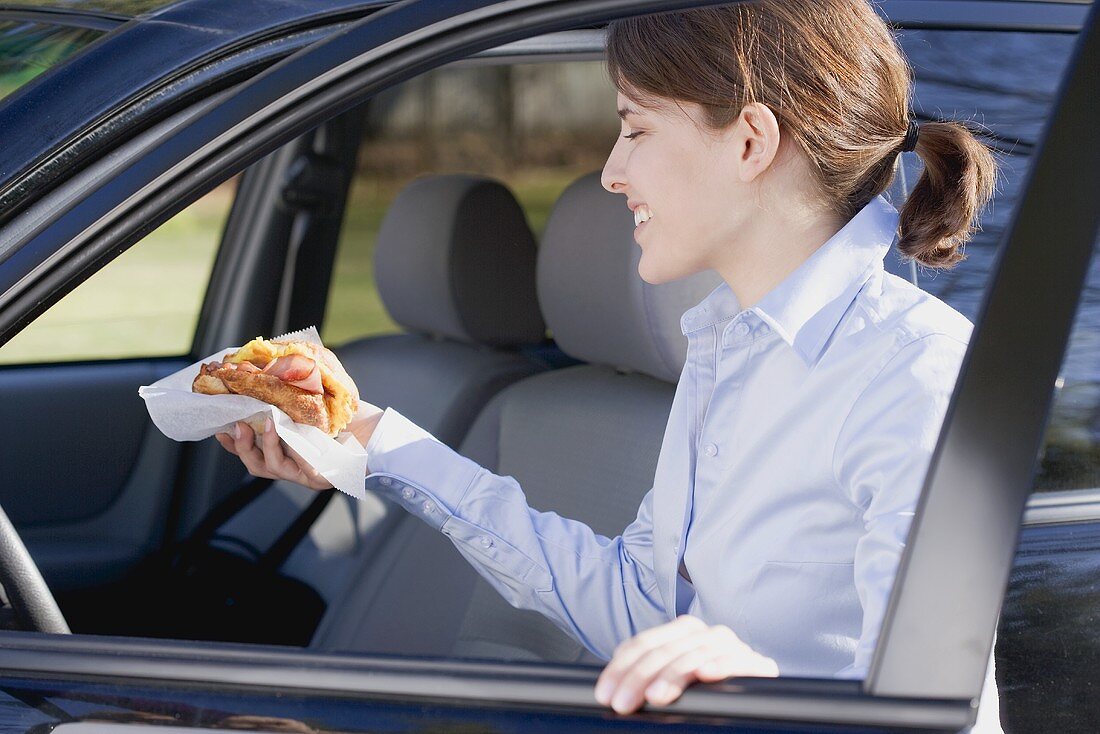 Junge Frau mit Croissant in der Hand steigt ins Auto