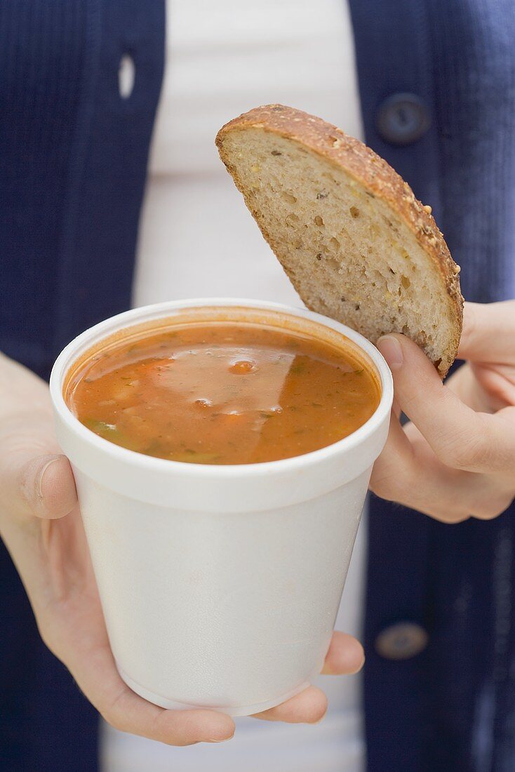 Frau hält Tomatensuppe und Brotscheibe