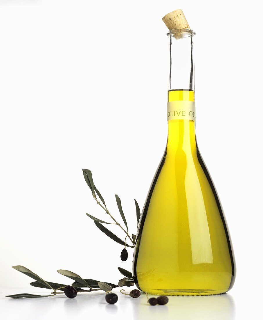 Olive oil in carafe, olive sprig beside it