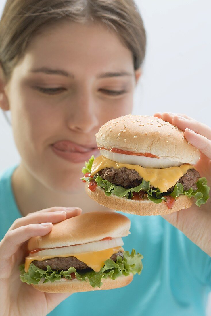 Junge Frau hält zwei saftige Cheeseburger