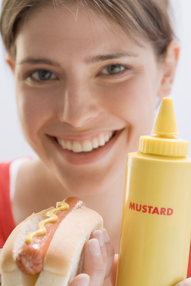Young woman holding hot dog and mustard bottle