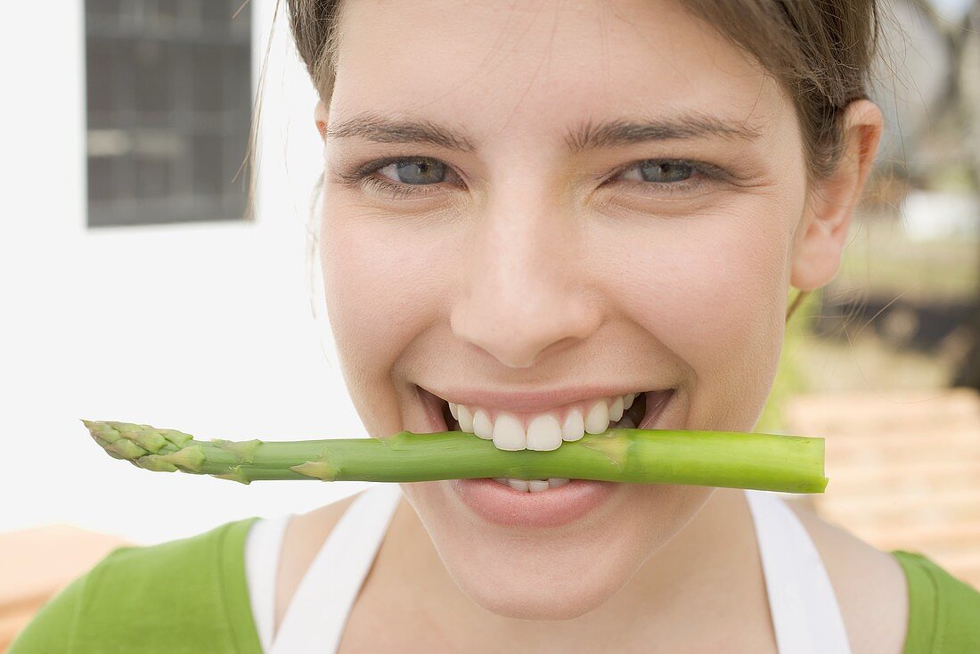 Young woman with an asparagus spear between her teeth