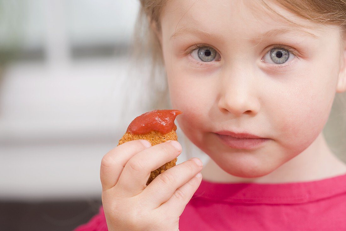 Little girl holding chicken nugget with ketchup
