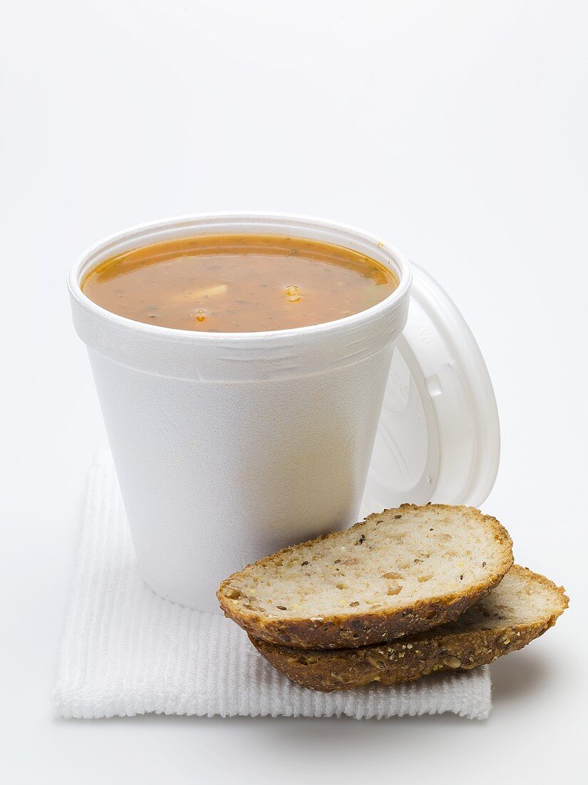 Tomato & vegetable soup in polystyrene cup, bread beside it