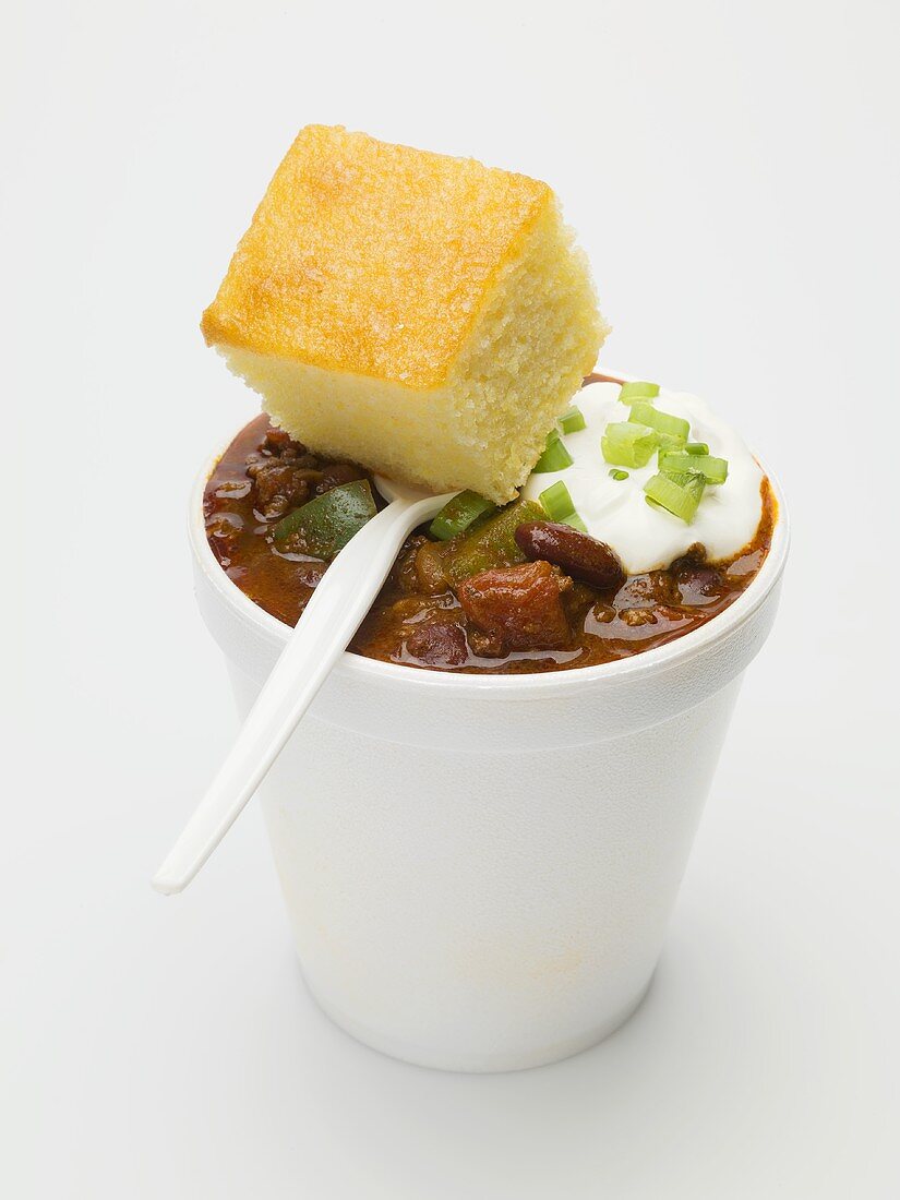 Chili con carne & sour cream in polystyrene cup, cornbread, spoon