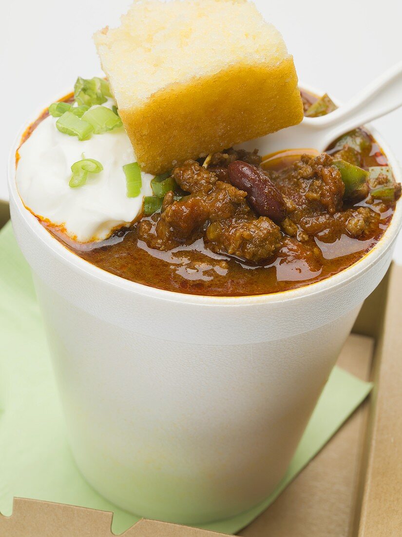 Chili con carne & sour cream in polystyrene cup, cornbread, spoon