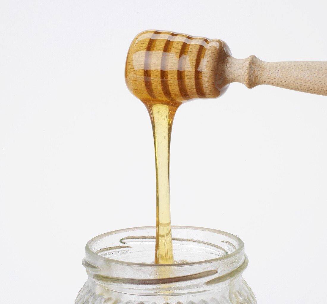 Honig fliesst vom Honiglöffel ins Glas