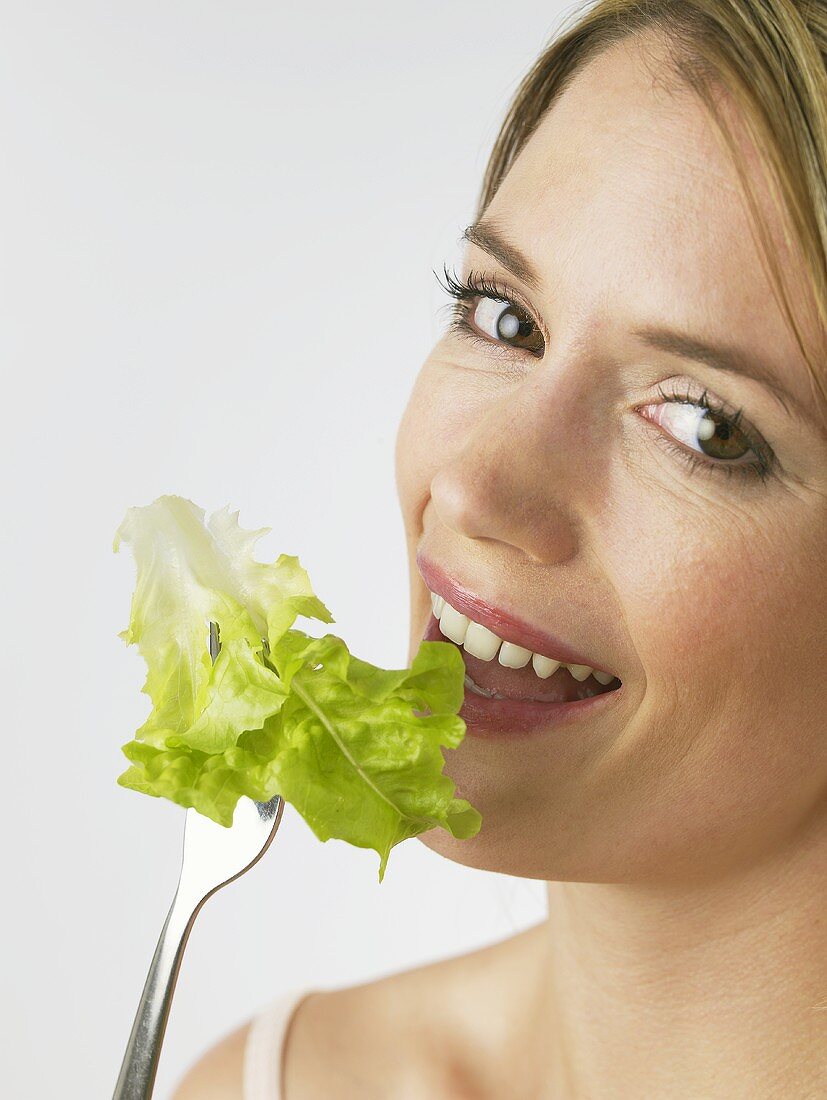 Frau beisst in ein Salatblatt auf Gabel