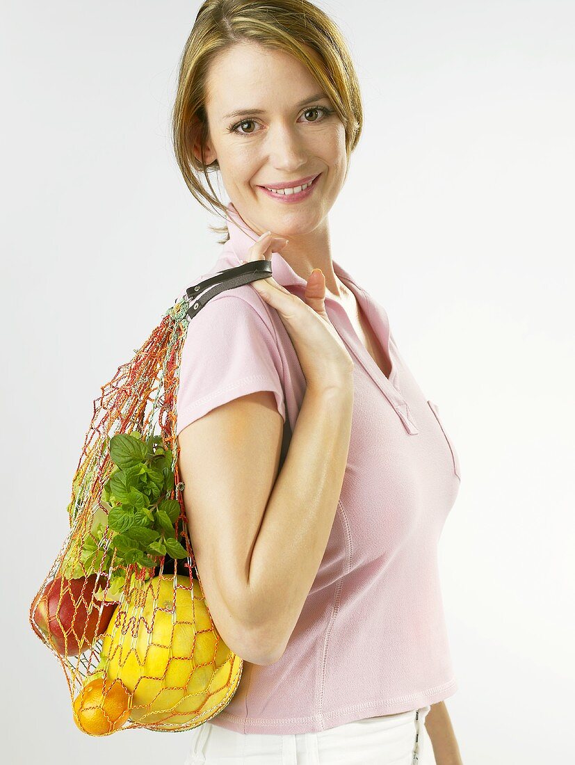 Frau hält Einkaufsnetz mit Früchten und Kräutern