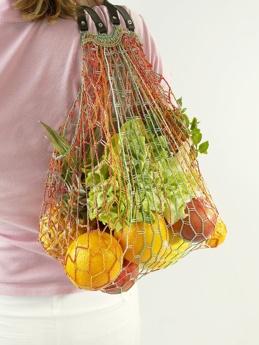 Woman holding string bag full of fruit and lettuce