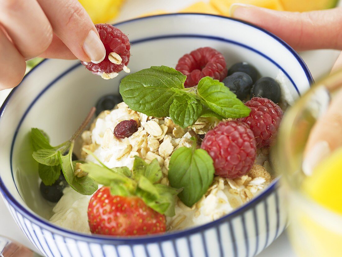 Hand taking a raspberry out of a bowl of muesli