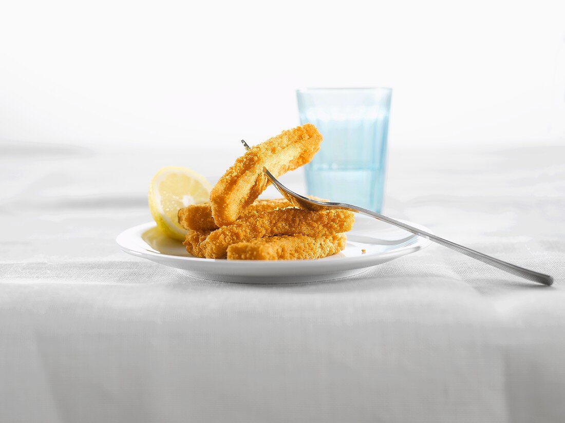 Fischstäbchen mit Zitrone auf Teller, Glas Wasser