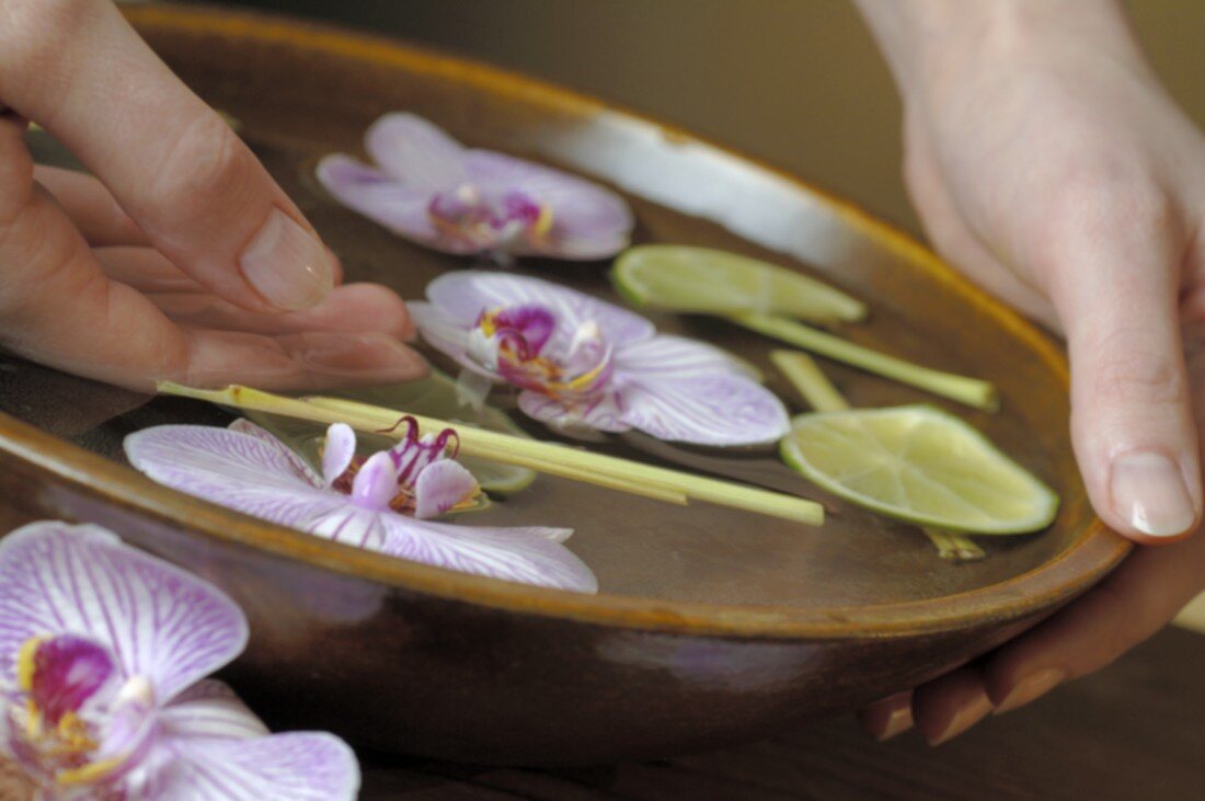 Woman with her hand in bowl of water with orchids & lime slices