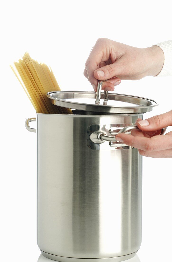 Hands holding spaghetti pan with lid