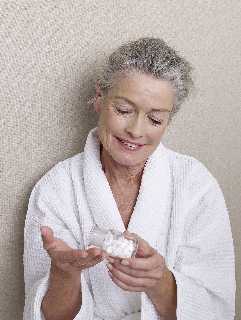 Mature woman in bathrobe holding bottle of tablets