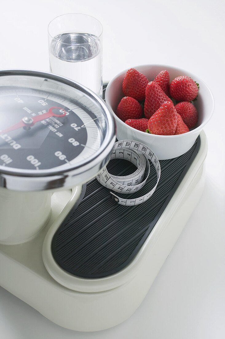 Strawberries, glass of water and tape measure on scales