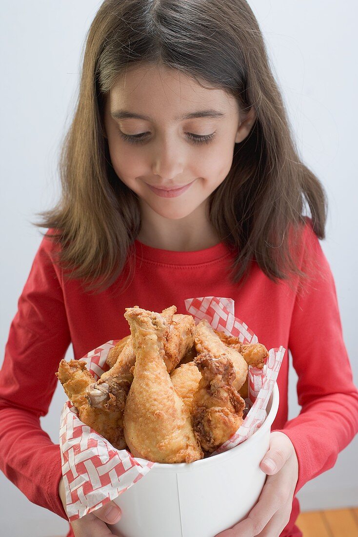 Kleines Mädchen hält frittierte Hähnchenkeulen
