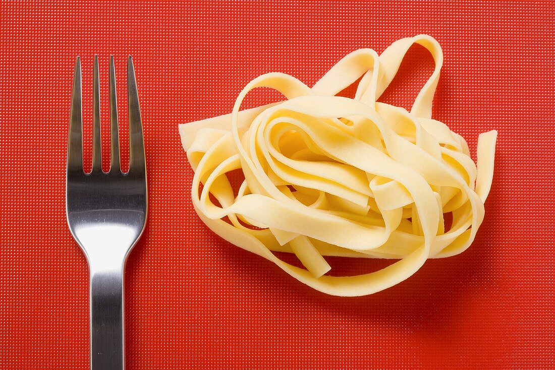 Ribbon pasta and fork on red background