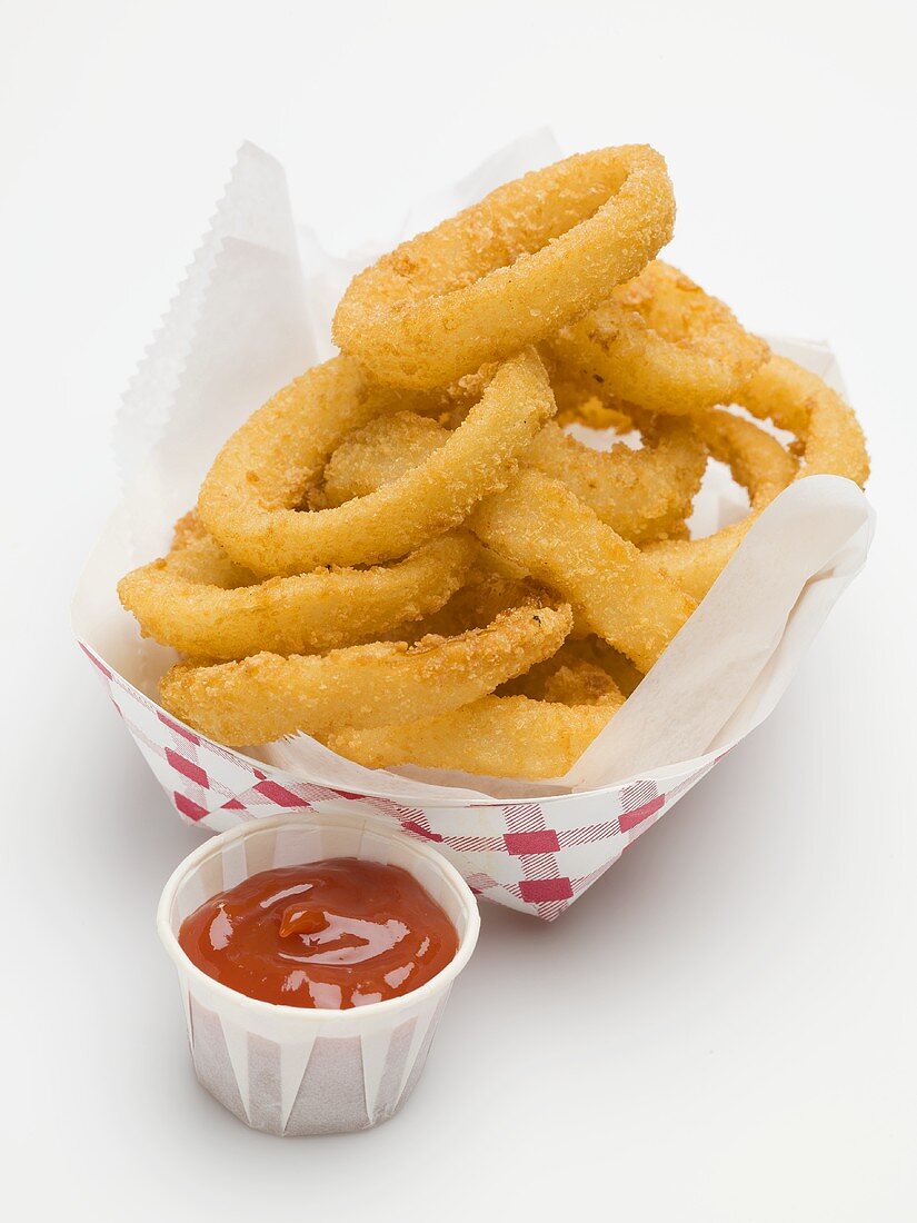 Frittierte Zwiebelringe im Pappschälchen, daneben Ketchup