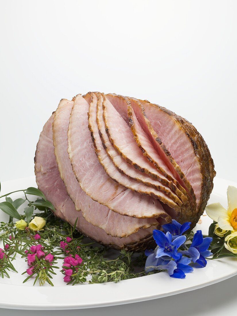 Roast ham, partly carved, on platter with edible flowers