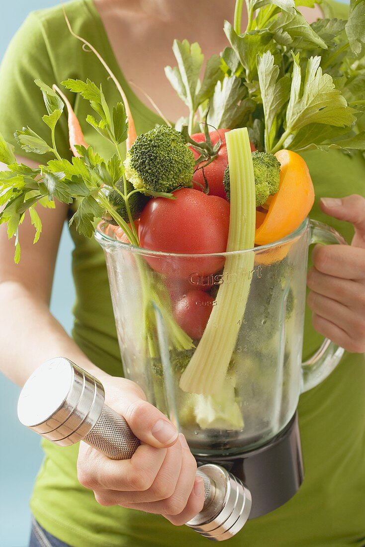 Woman holding hand weight & fresh vegetables in liquidiser