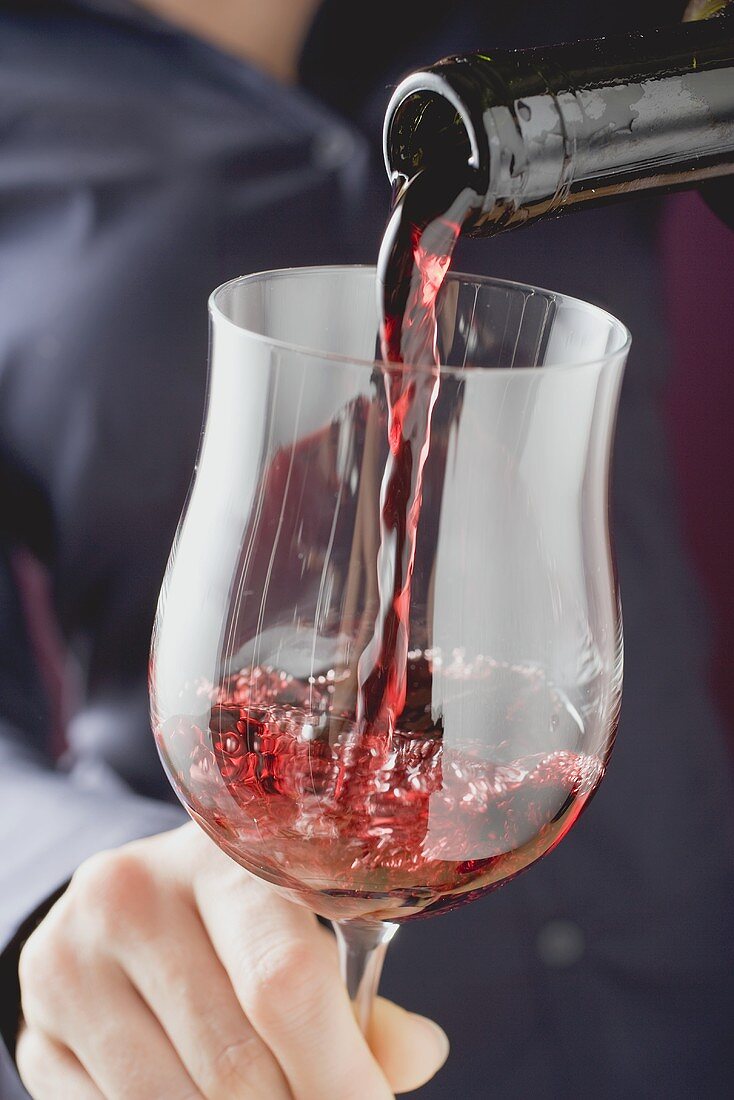 Person schenkt Rotwein in Glas ein