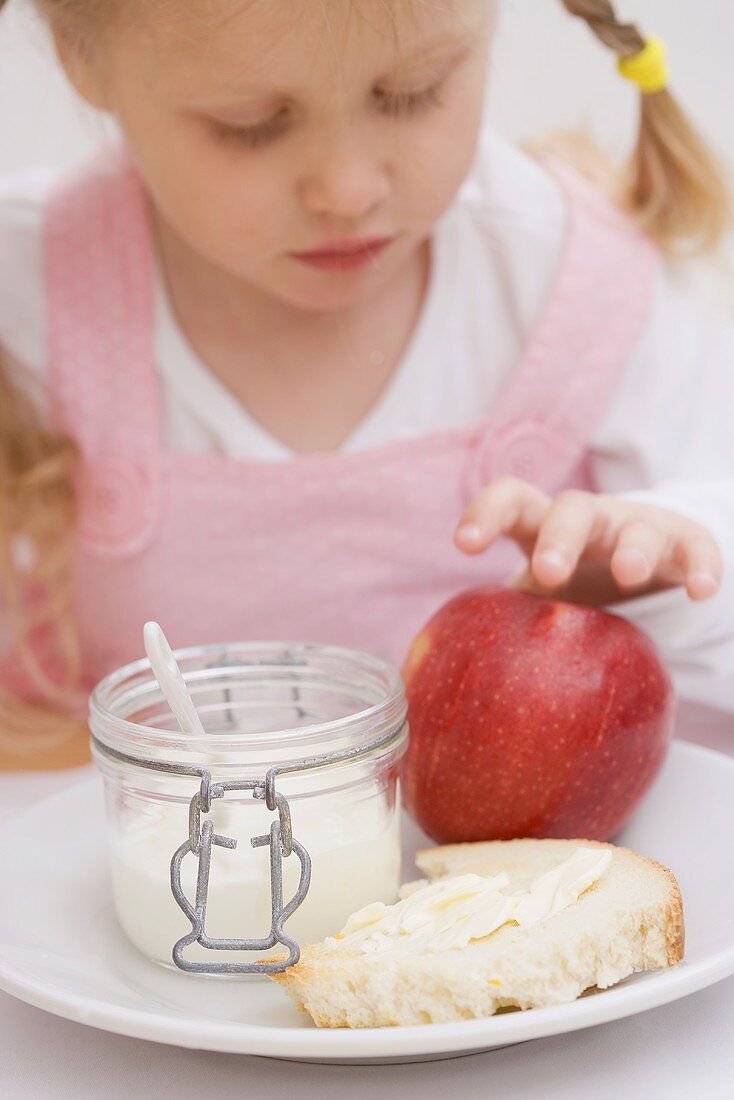 Kleines Mädchen mit Apfel, Joghurt und Butterbrot