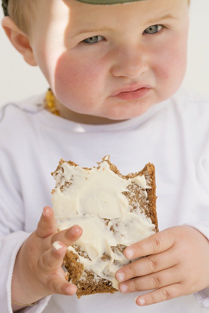 Baby holding a partly-eaten slice of bread and butter
